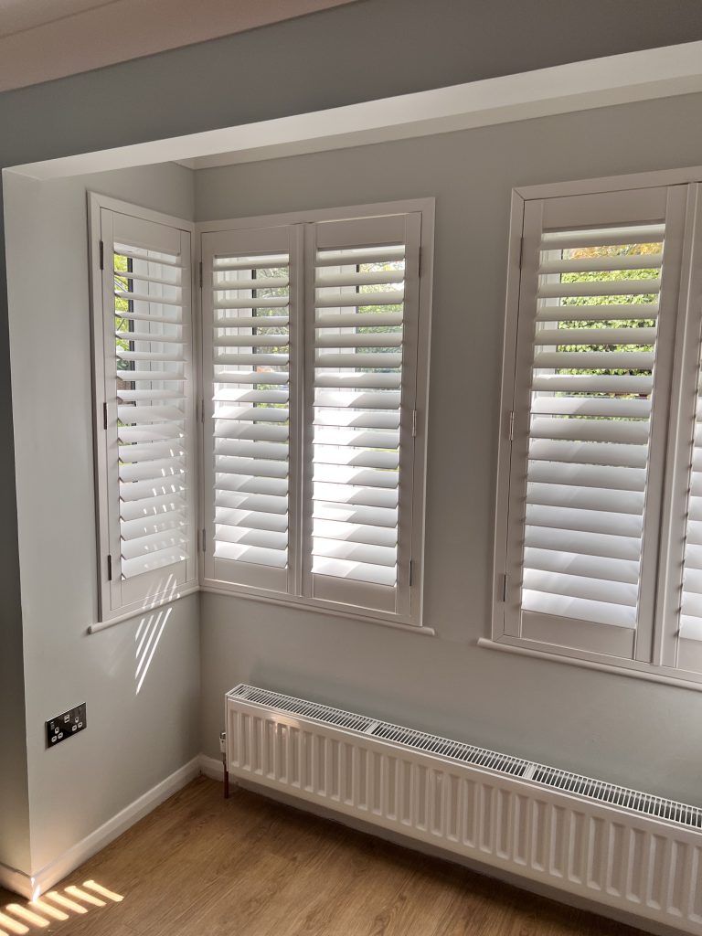 olets intérieurs blancs sur mesure style plantation pour fenêtres d'angle, lumière filtrant à travers les lamelles, Persiennes plantations de Intérieurs Inspirés.