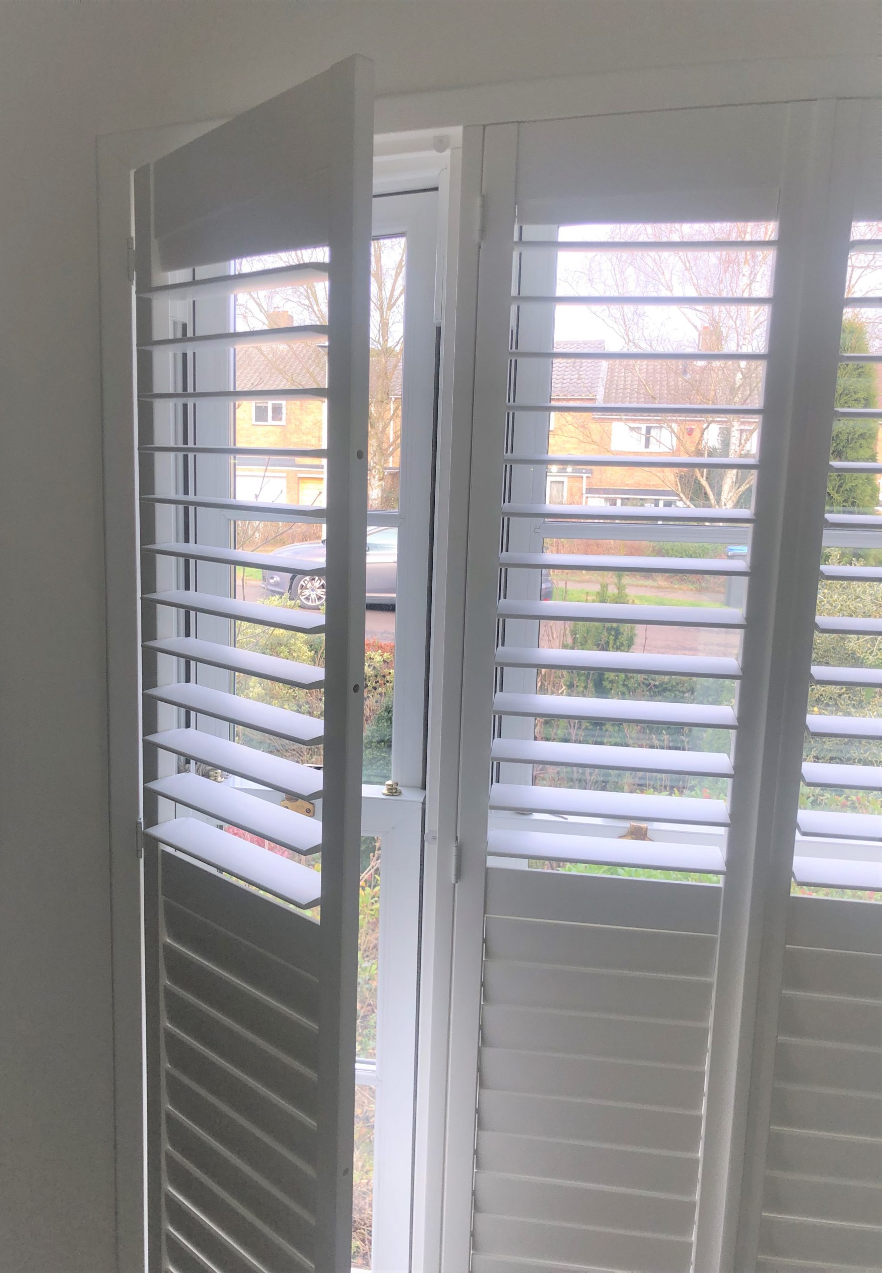 Persiennes plantation blanches sur mesure avec un panneau ouvert vers l'intérieur, montrant la fonctionnalité et la fenêtre, Intérieurs Inspirés.