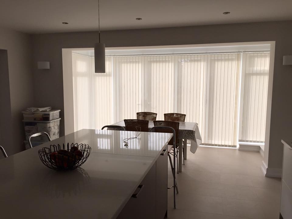 Stores verticaux sur mesure de couleur neutre installés sur une grande baie vitrée dans un espace de vie moderne, Intérieurs Inspirés.